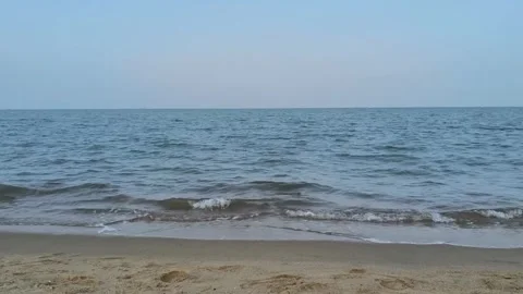 Serene view of the calm ocean waves gently rolling onto the sandy beach at dusk Stockbeeldmateriaal 334163742