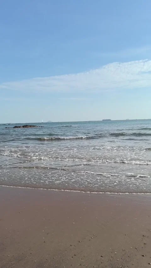 A serene view of gentle ocean waves rolling onto a sandy beach under a clear Vídeos de archivo 334163211