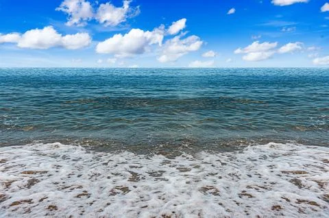 A serene view of ocean waves gently washing onto a sandy beach under a bright Stock Photos