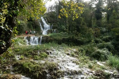 A serene waterfall cascades down multiple levels of lush, green vegetation Stock Photos