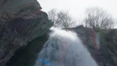 A serene waterfall cascading down rugged rocks, surrounded by lush greenery 스톡 동영상 314456403