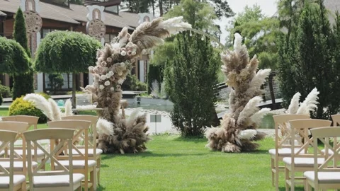 A serene wedding setup with chairs on lush lawn and a floral arch Stock Footage 306361228
