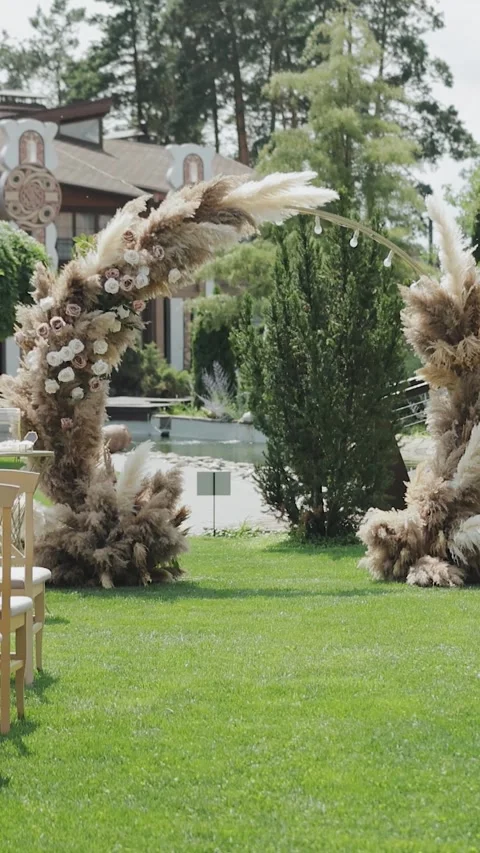 A serene wedding setup with chairs on lush lawn and a floral arch. Vertical Stock Footage 308396256