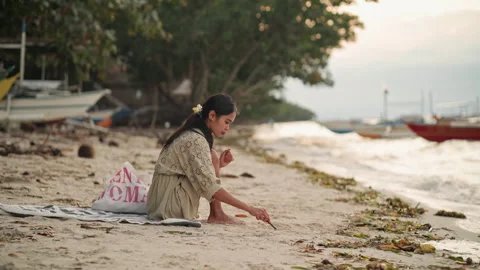 Serene woman observing shells and gentle waves on calm beachfront. Calm and Stock Footage 341669113