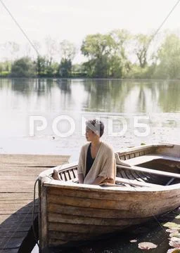 Serene woman sitting in canoe at sunny lakeside dock Stock Photos