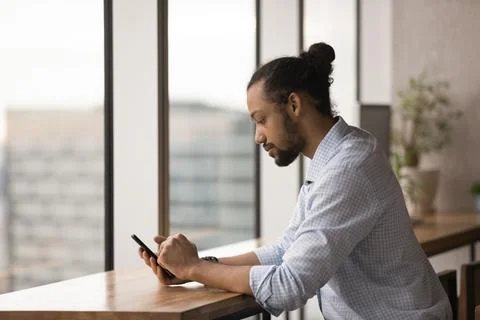 Serious African businessman sit at workplace hold smartphone check e-mail Stock Photos