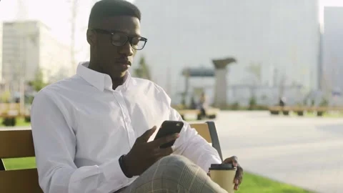 Serious african guy is sitting on bench in park and writing notes in notebook. Stock Footage 131018737