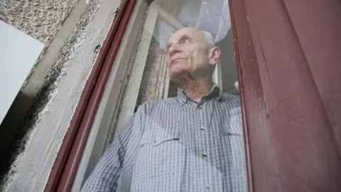 Serious aged man looks through brown outdated window 스톡 동영상 157356849
