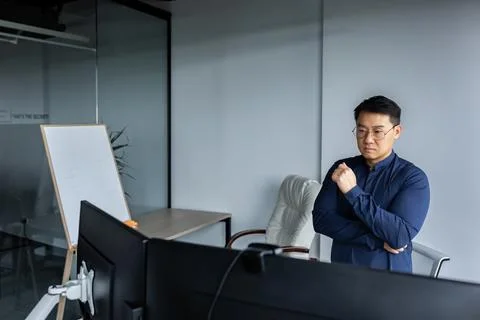 Serious and thinking asian engineer looking at two monitors, close-up photo of Foto stock