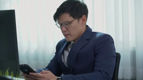 Serious asian business man using mobile phone on desk in office Stock Footage 252821906