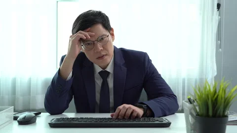 Serious asian business man using computer on desk in office hands on forehead Stock Footage 252825077