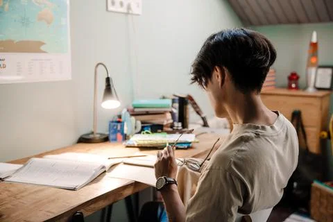 Serious asian guy studying with book while sitting at desk at home Stock Photos