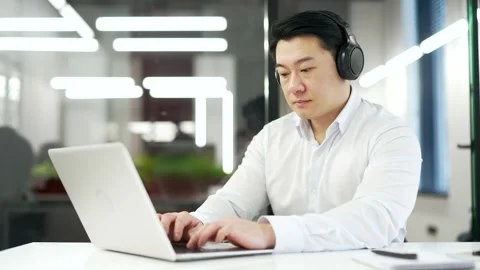 Serious asian IT specialist coder in wireless headphones typing on laptop comput Stock Footage 269392763