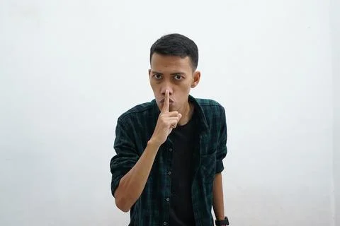 Serious asian man wearing dark green casual wear holding finger near lips, .. Stock Photos