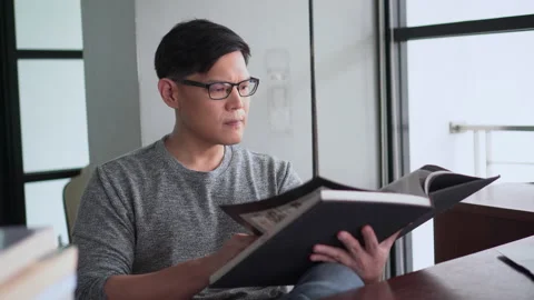 Serious asian young man reading a book in Living room at home Stock Footage 158790693