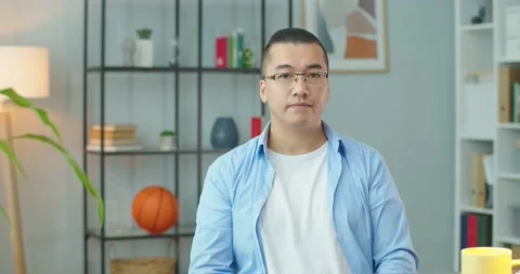Serious asiat man looking to camera. Slightly confused man in glasses in home Stock Footage 156035888