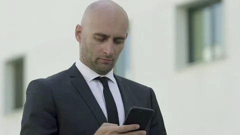 Serious bald man in suit using smartphone and typing Video stock 136742478