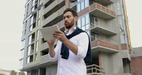 Serious bearded guy holding digital tablet outdoor and controlling construction Stock Footage 140681586
