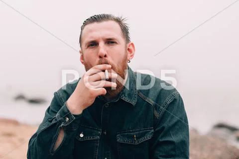 Serious bearded man smoking a cigarette on the beach Stock Photos