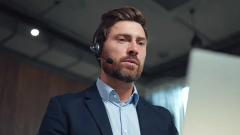 Serious bearded man in wireless headset talking during video chat on laptop Stock Footage 251721626