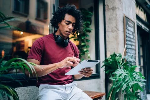 Serious black man browsing tablet on bench near cafe Stock Photos