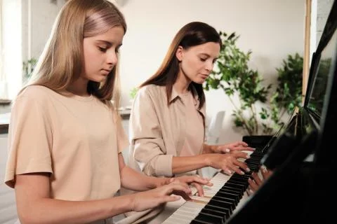 Serious blond teenage girl pushing keys of piano during home lesson of music Stock Photos