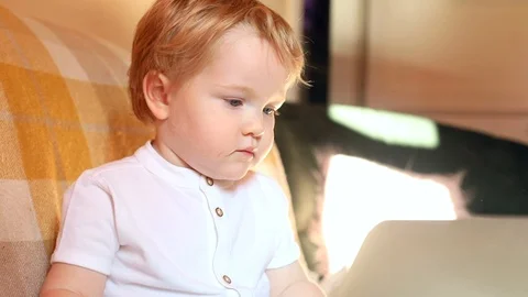 Serious blonde baby boy using laptop computer with sunlight on background Vídeos de archivo 99771395