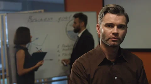 Serious boss posing on a camera while his colleagues discuss totally new project Stock Footage 68335611