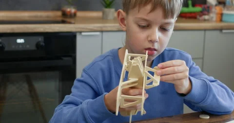 Serious boy attaches small wheels to airplane playing at desk Stock Footage 323973640