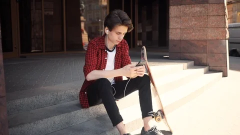 Serious boy look at camera using mobile phone with headphones keeps skate guy Stock Footage 92051671