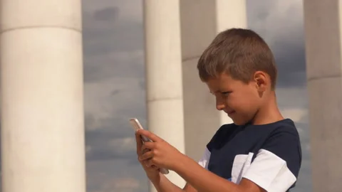 The serious boy is looking on the phone screen outdoors Stock Footage 156058704