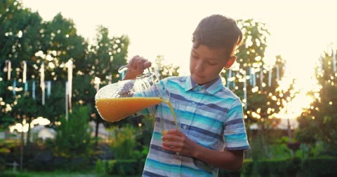 Serious boy pour orange juice in the glass at sunset Stock Footage 239855448