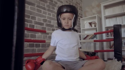 Serious boy in red Boxing Gloves and black Head guard sitting in his bed Stock Footage 111547564