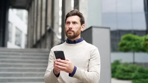 A serious businessman is using a phone while standing on the street near  Stock Footage 301542200