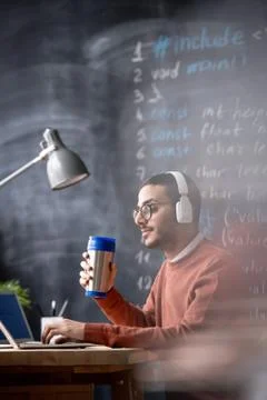 Serious busy manager or programmer in headphones having drink by laptop Foto stock