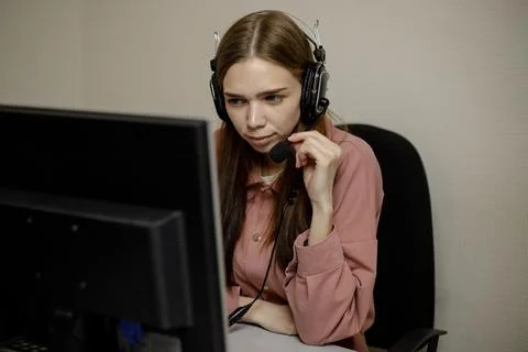 A serious call center operator is talking to a client while looking at a comp Stock Photos
