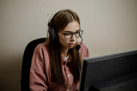 A serious call center operator is talking to a client while looking at a comp Stock Photos