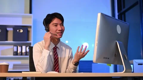 Serious call center operator in wireless headset talking with customer, Asi.. Stock Footage 313578055