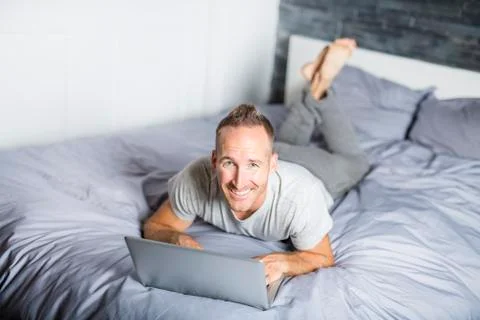 Serious casual young man using laptop in bed at home Stock-Fotos