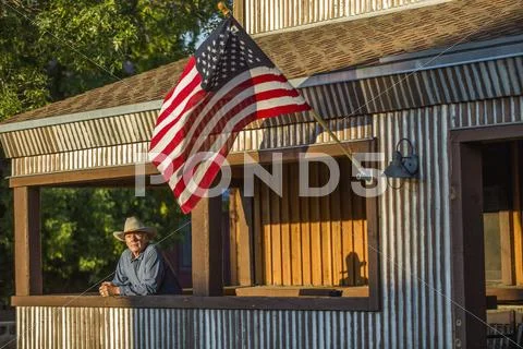 Serious Caucasian farmer on porch with American flag Stock-Fotos
