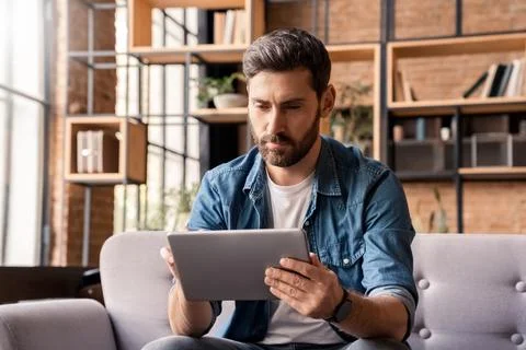 Serious caucasian man using digital tablet sitting on sofa at home office Stock Photos