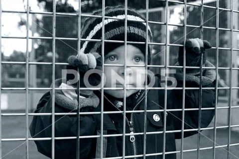 Serious child looking through fence Stock Photos