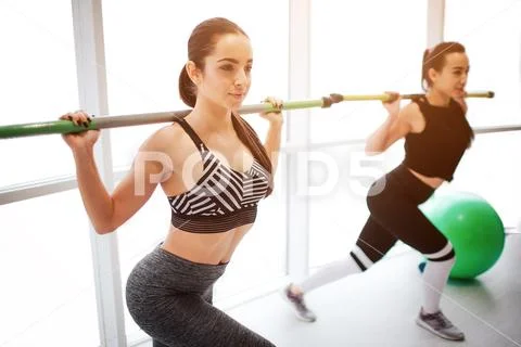 Serious concentrated young women exercising in fitness room together. They Stock Photos