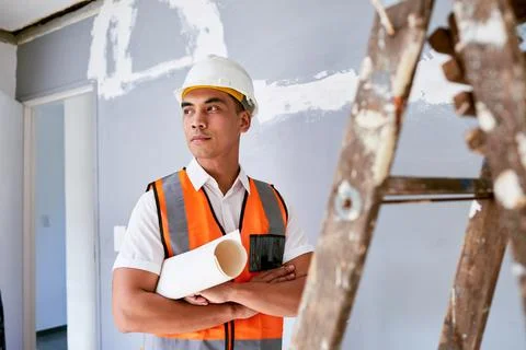 A serious construction worker stands with plans under his arm at home renovation Stock Photos