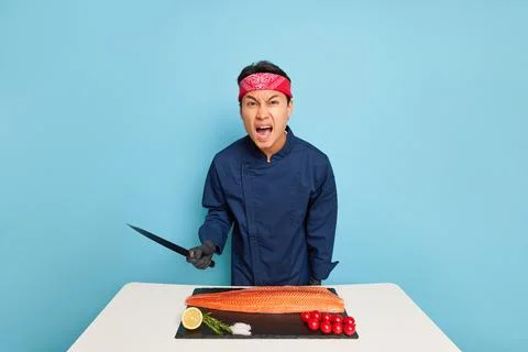 Serious cook going to slice fish fillet, holding knife in his hand, standing Stock Photos