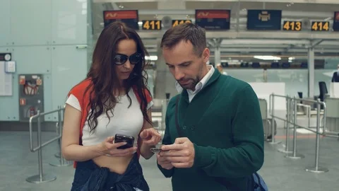 Serious couple checking the time of flight on phone, standing in the hall of Stock Footage 108868829