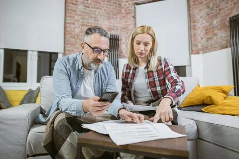 Serious couple with mobile and documents counting finances Stock Photos