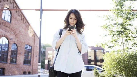 Serious dark haired walking and web surfing from her smartphone Stock Footage 84614681
