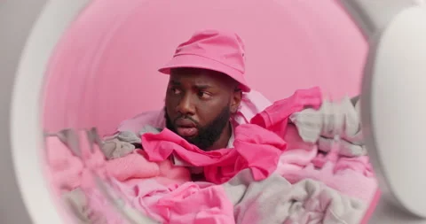 Serious dark skinned man covered with laundry poses from inside of washine Stock Footage 156967312