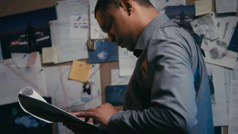 Serious detective reading interrogation protocol looking at crime evidence board Stock Footage 234898980